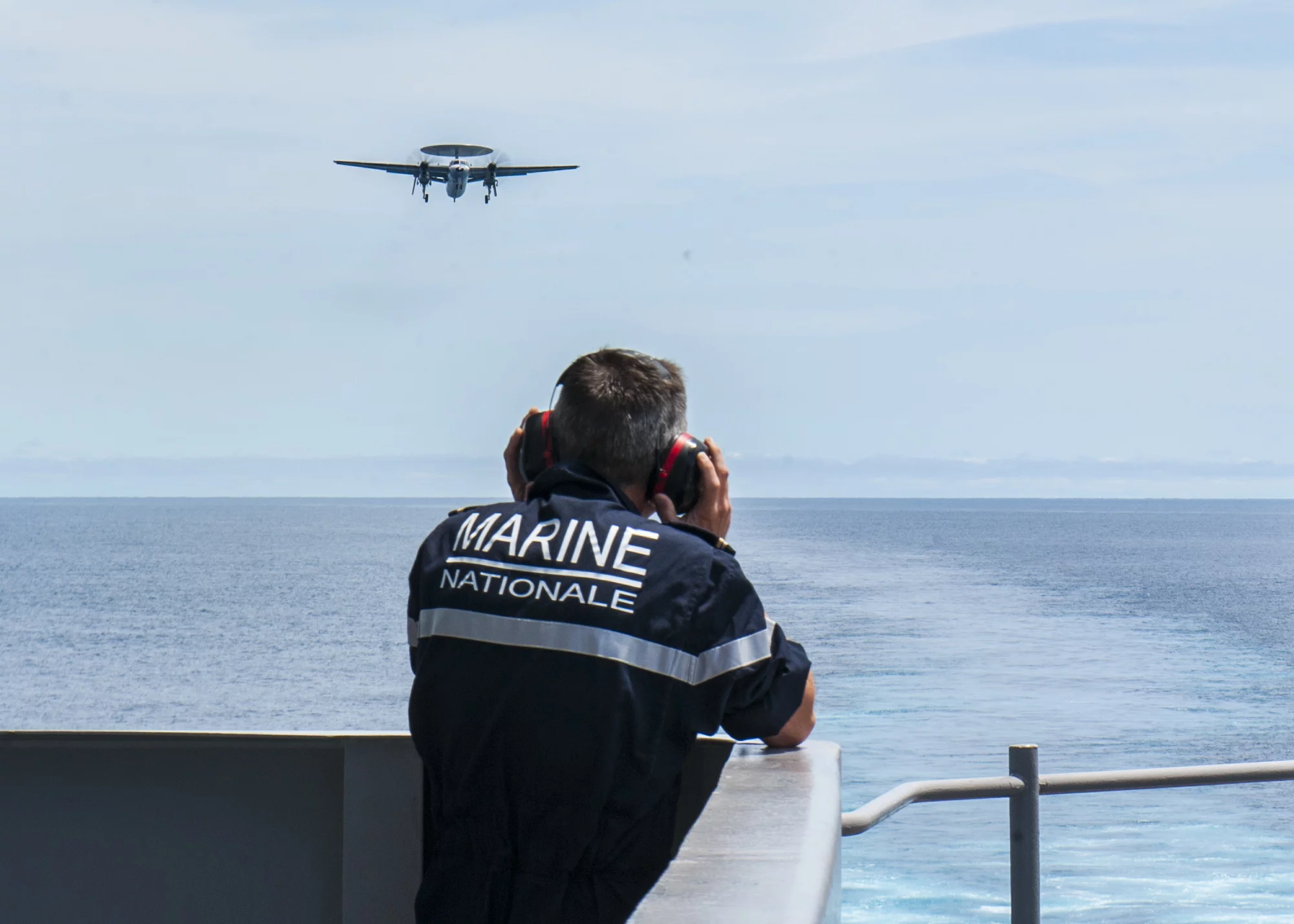 Un marin français observe l'approche d'un avion de guet Hawckeye E-2C sur le pont de l'USS George H.W. Bush